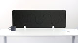 Black wave-shaped desk divider with three curved sections mounted on a white desk surface.