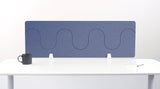 Blue wave-patterned desk divider with white mounting brackets shown on white desk with coffee mug and papers.