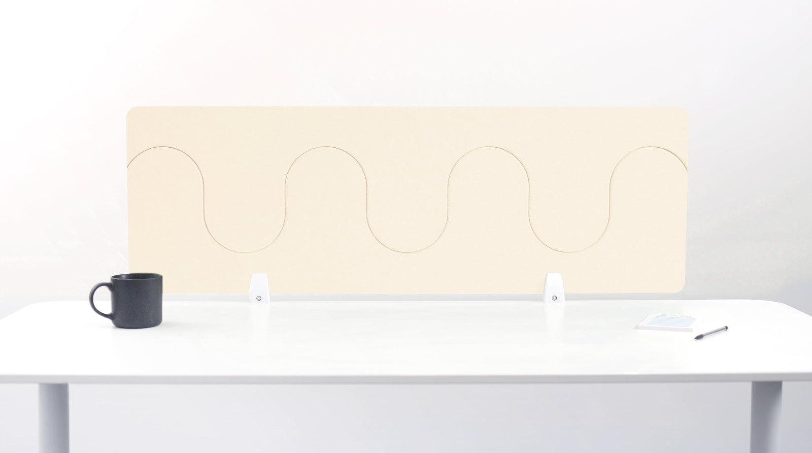 An ivory-colored felt desk divider placed on a white desk with a black mug and a pen beside it.