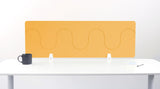 Yellow wave-patterned desk divider with rounded cutouts mounted on white desk with black mug and notepad.