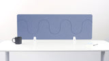 Blue wave-patterned desk divider with white mounting brackets displayed on white desk with mug and supplies.