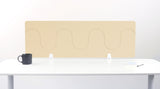 Beige desk divider with wavy cutout pattern mounted on white desk with black mug and office supplies.