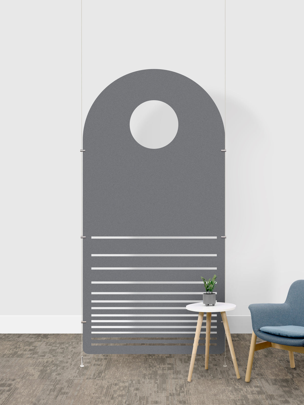 A minimalist arched room divider in a light gray color, featuring a circular cutout at the top and horizontal slats on the lower half. The divider is shown in a modern room setting with a small white side table, a potted plant, and a blue armchair against a white wall.