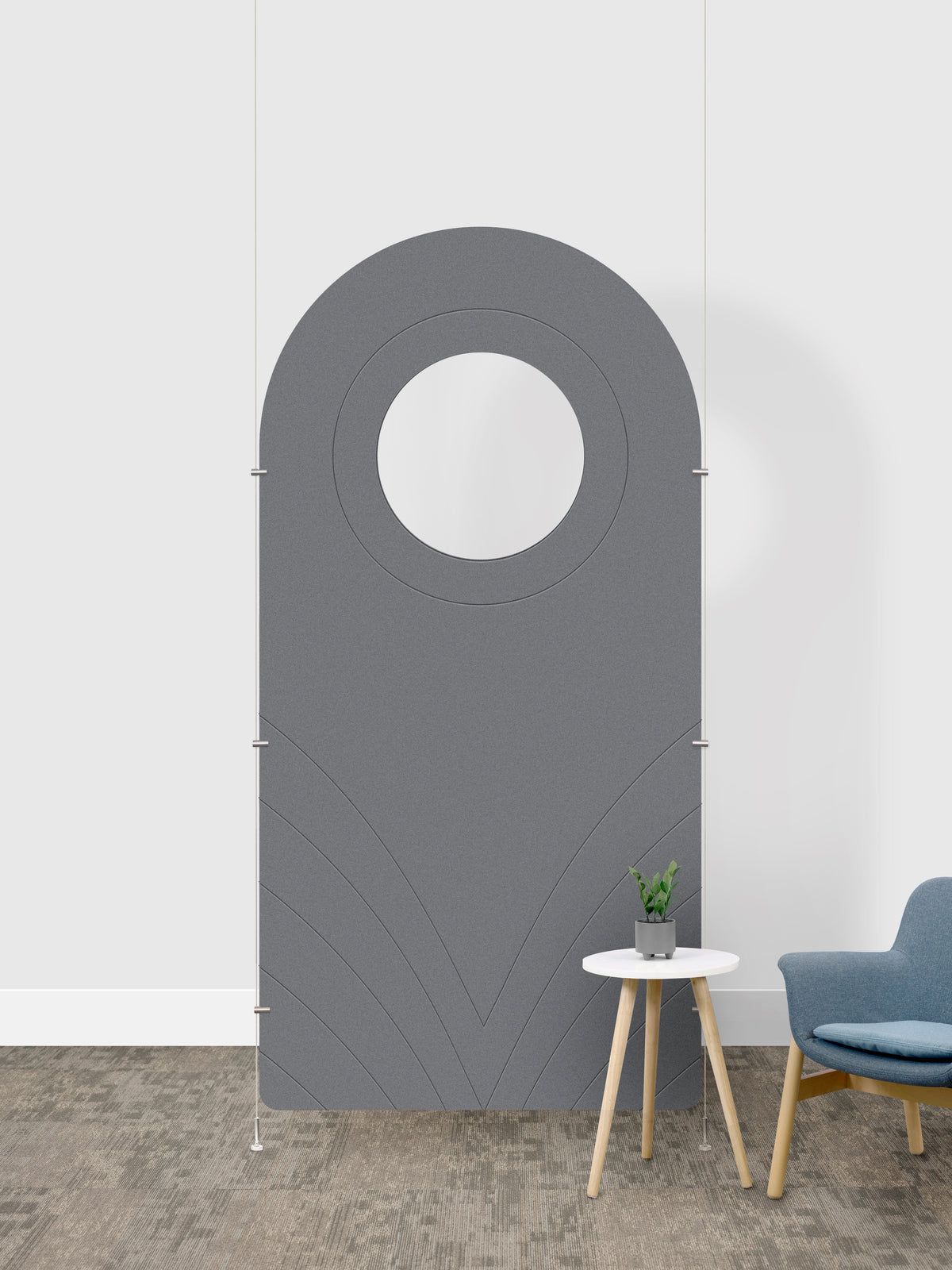 A gray arched room divider panel with a circular cutout in the center, shown in a room setting next to a small side table and a blue chair.