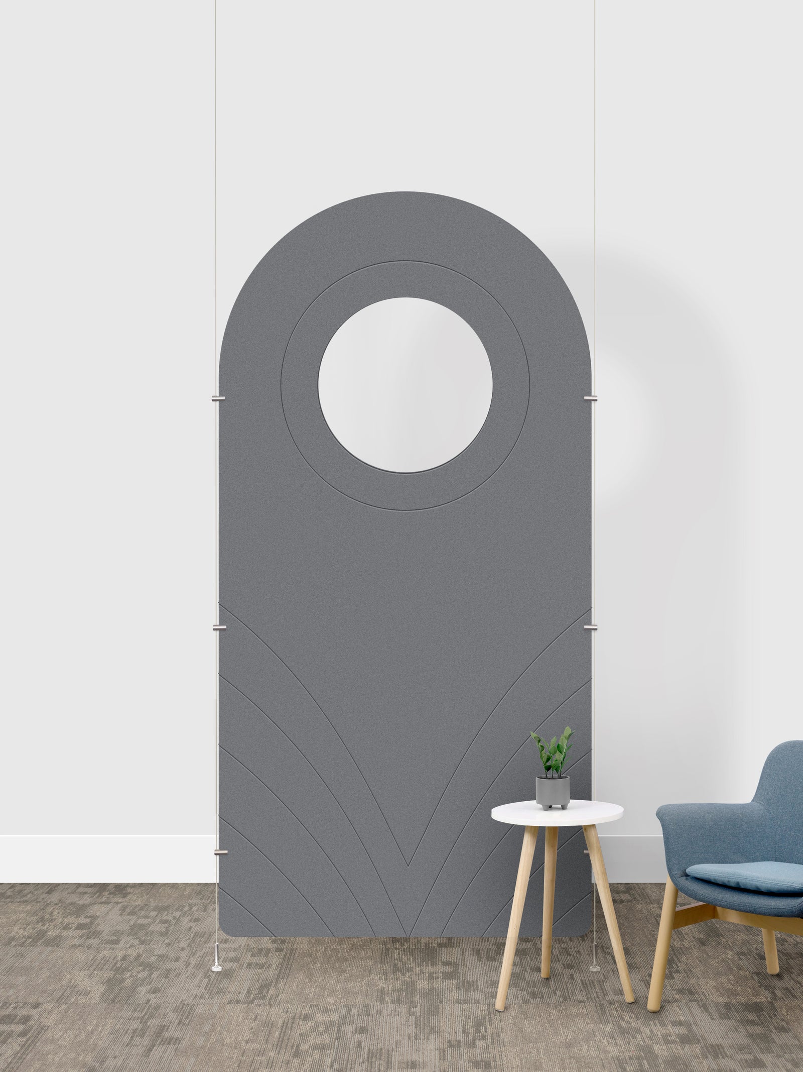 A gray arched room divider panel with a circular cutout in the center, shown in a room setting next to a small side table and a blue chair.