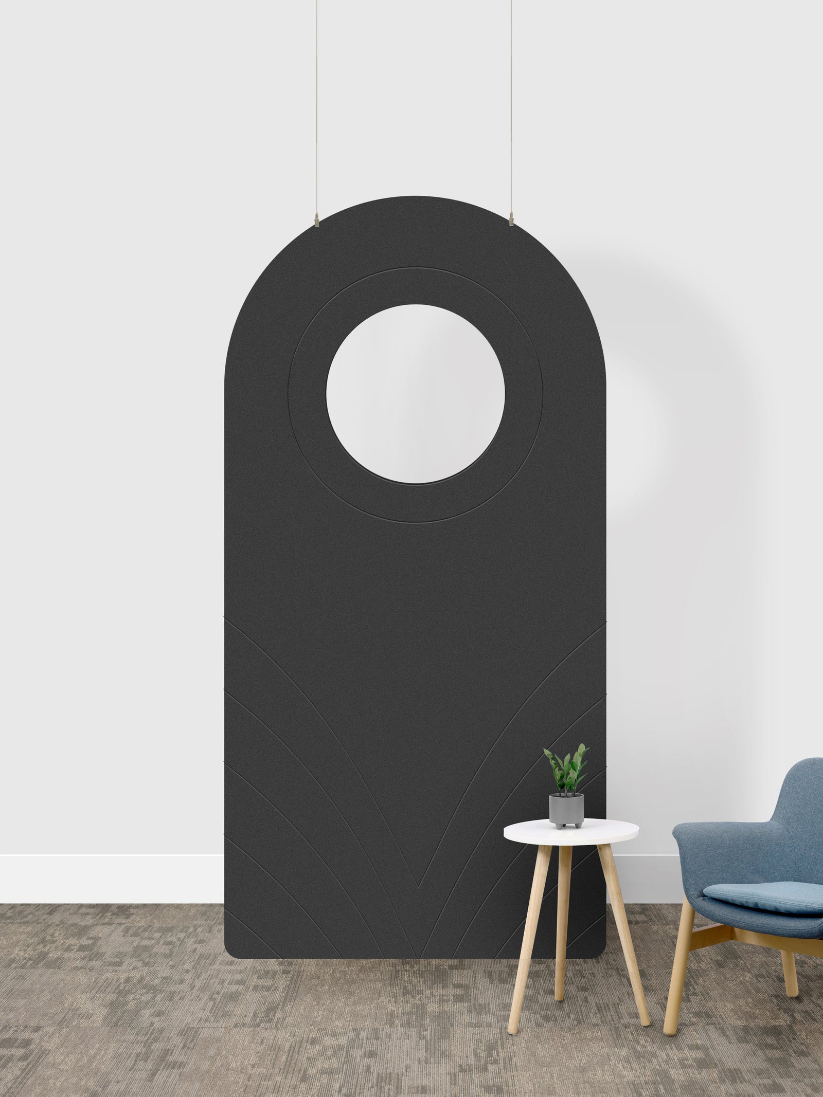 A dark gray arched room divider panel with a circular cutout in the center, shown in a room setting next to a small side table and a blue chair.
