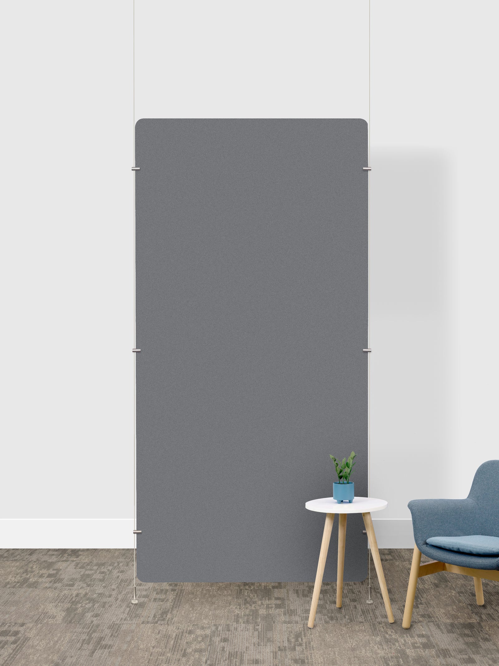 A large, minimalist gray rectangular room divider in a modern room setting with a white wall, textured gray floor, a small white side table with a potted plant, and a blue armchair.