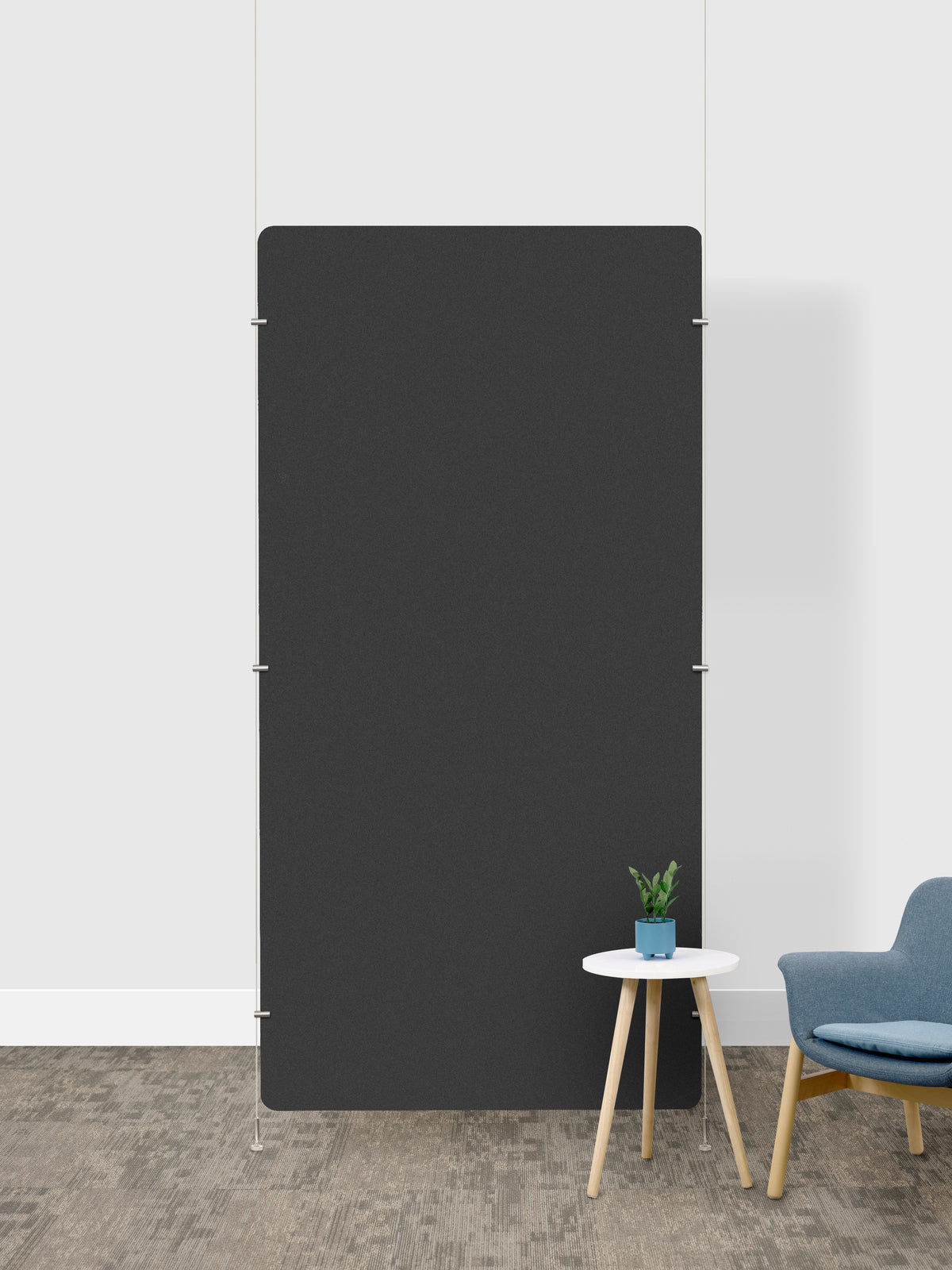 A large, minimalist charcoal gray rectangular room divider in a modern room setting with a white wall, textured gray floor, a small white side table with a potted plant, and a blue armchair.