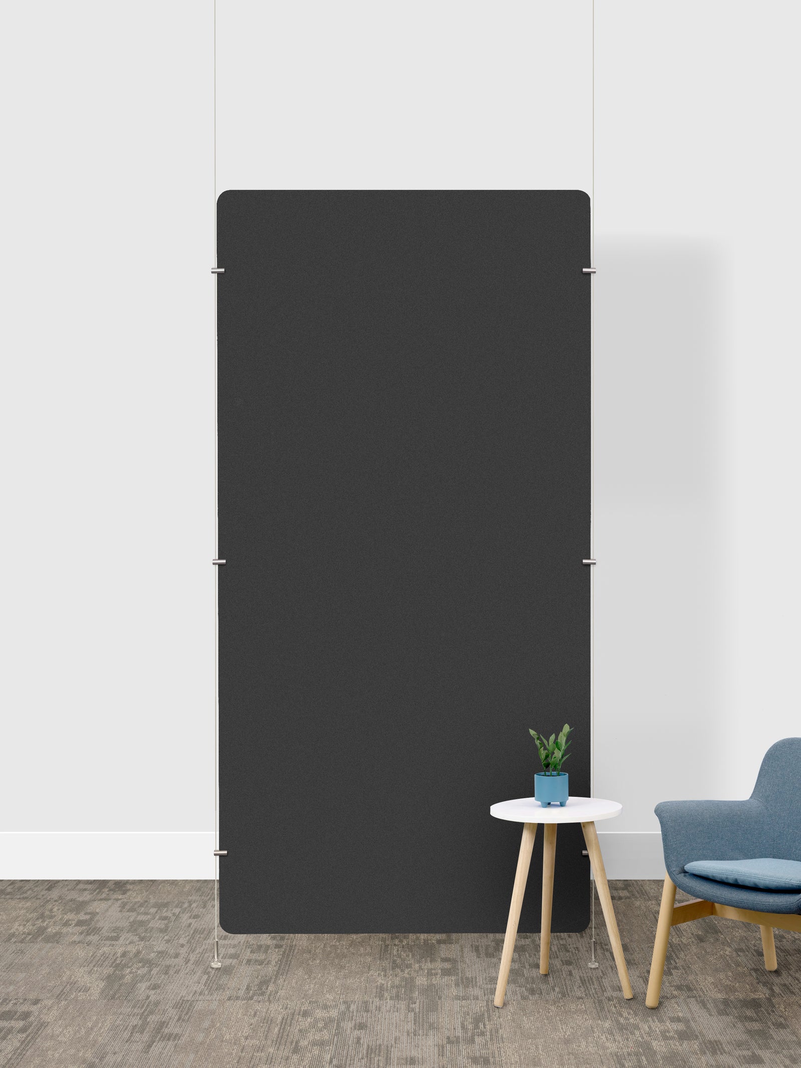 A large, minimalist charcoal gray rectangular room divider in a modern room setting with a white wall, textured gray floor, a small white side table with a potted plant, and a blue armchair.