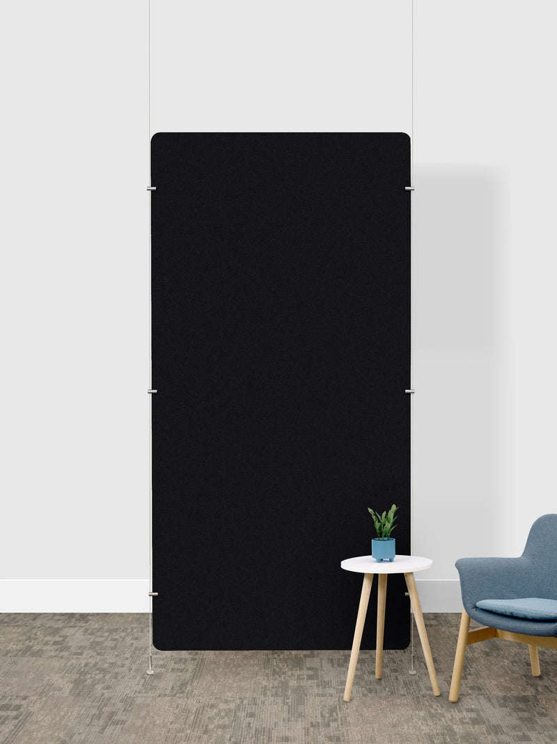A large, minimalist black rectangular room divider in a modern room setting with a white wall, textured gray floor, a small white side table with a potted plant, and a blue armchair.