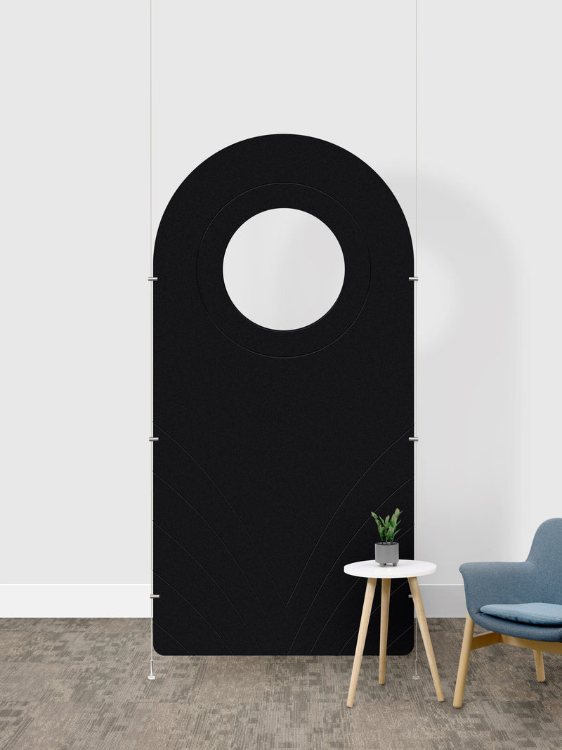 A black arched room divider panel with a circular cutout in the center, shown in a room setting next to a small side table and a blue chair.