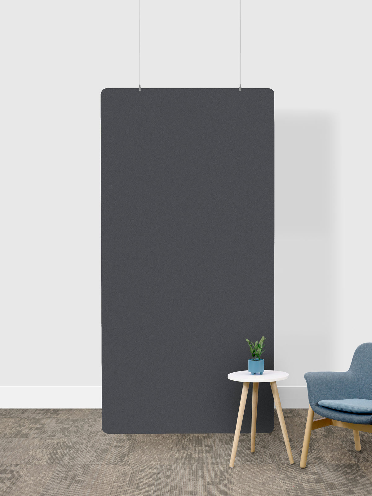 A large, minimalist dark gray room divider hanging against a white wall in a modern room setting, with a small white side table and a blue armchair below.