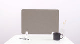 Gray desk divider with rounded corners mounted on white brackets on a desk with pens, mug, and vase.