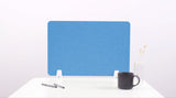 Blue desk divider with white mounting brackets on white desk, styled with pens, mug, and vase.