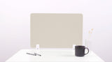 Beige desk divider with white mounting brackets on white desk surface, styled with pens, dark mug, and vase.