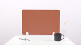 Rust-colored rectangular desk divider with white mounting brackets, positioned on white desk with coffee mug and pens.