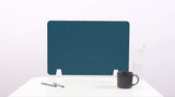 Teal desk divider panel with white base clamps, positioned on white surface with pens, mug, and vase.