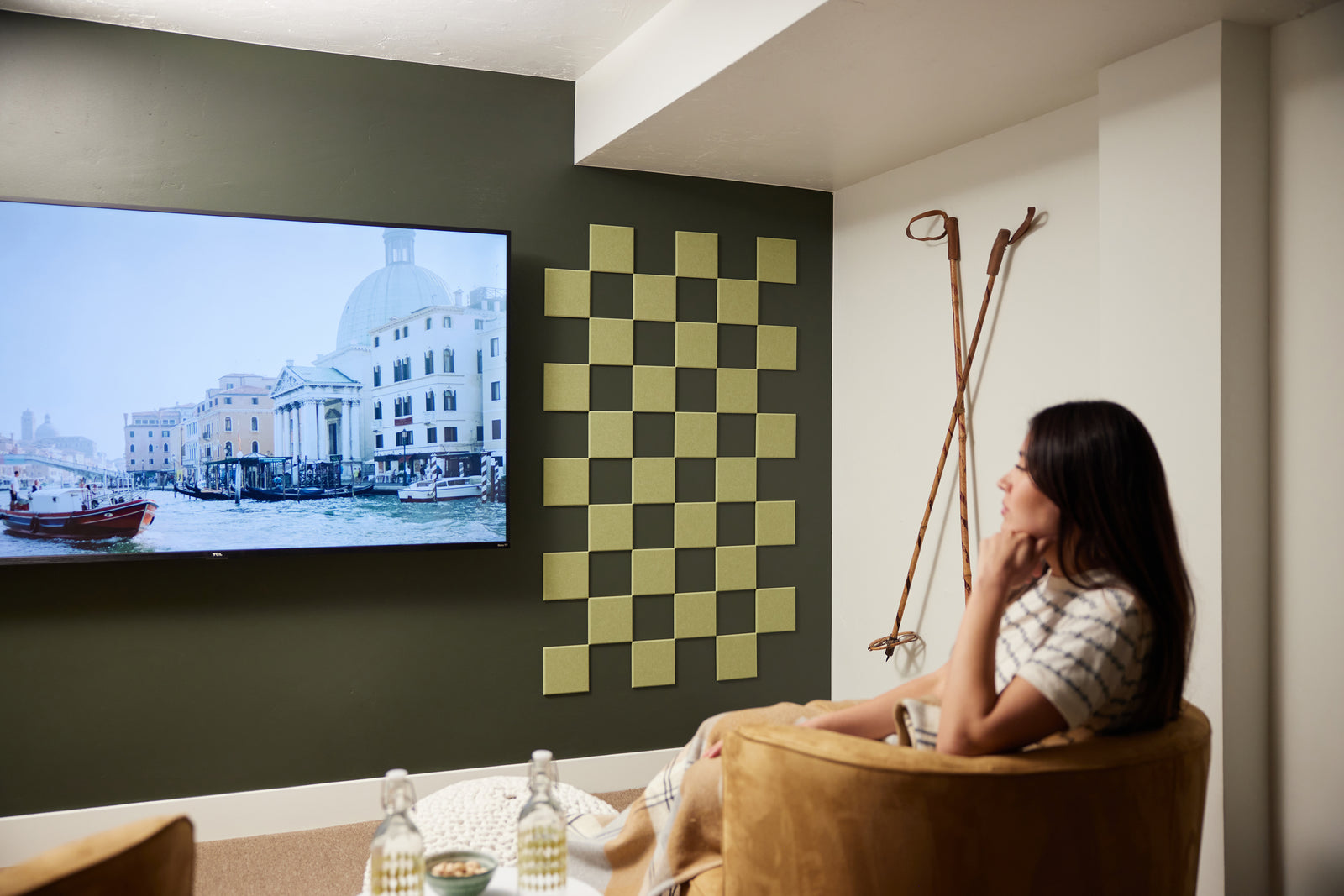 A Felt Right wall art design in a shade of green square felt tiles in a checkered pattern on a darker green wall next to a tv