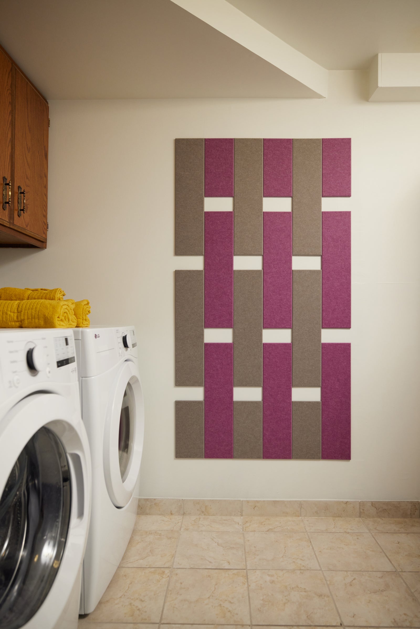 A Felt Right wall art design in shades of brown and pink on a white wall in a laundry room with a washer and a dryer