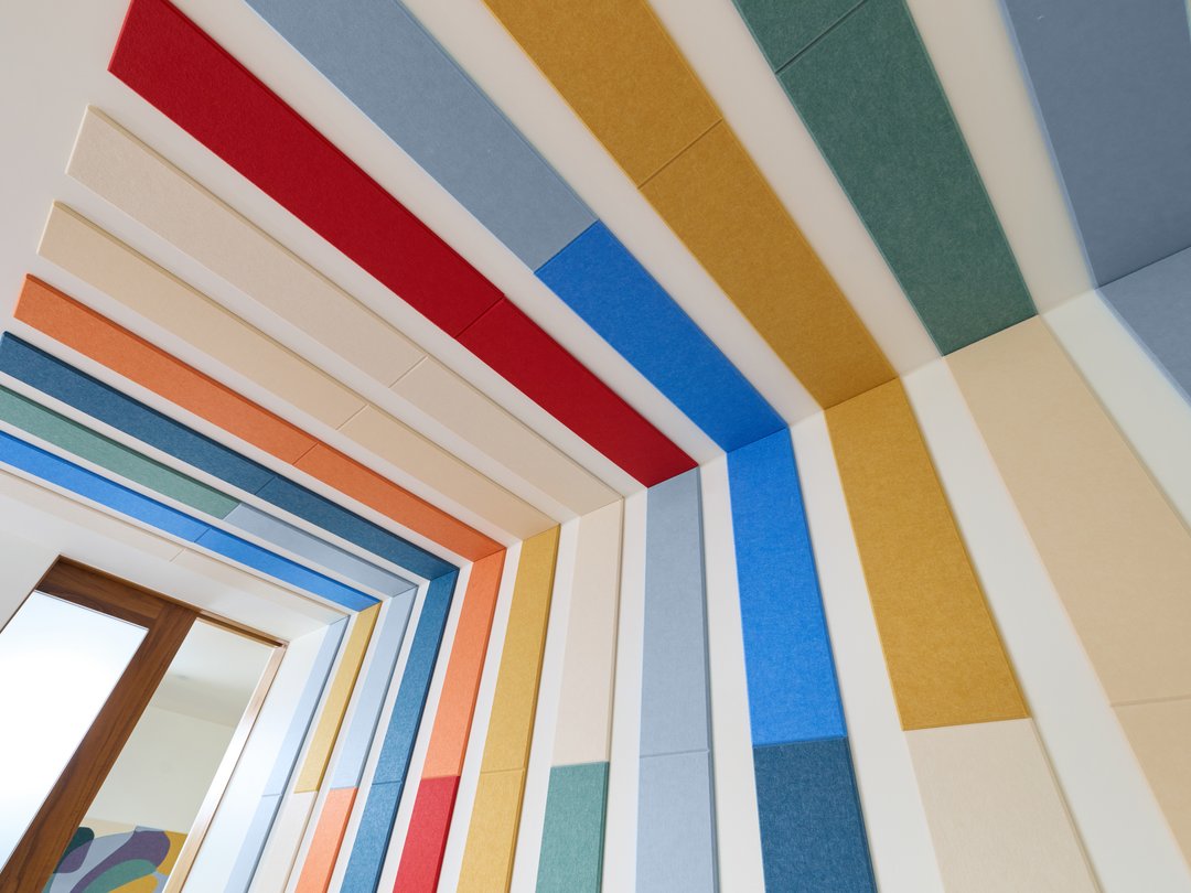 Felt right wall art design in a bedroom using shades of red, orange, blue, and cream felt tiles on a white wall and ceiling.