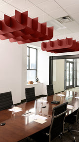 Red 3D cloud-shaped acoustic baffles suspended from ceiling in conference room above wooden table.