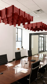 Red 3D cloud-shaped acoustic baffle suspended from ceiling in conference room above wooden table.