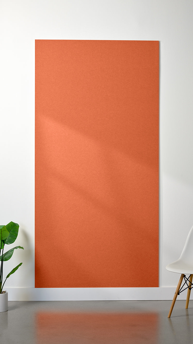 Orange Felt Right 4’ x 8’ PET felt panel with no engraving against a white wall. A plant and chair are in the foreground.
