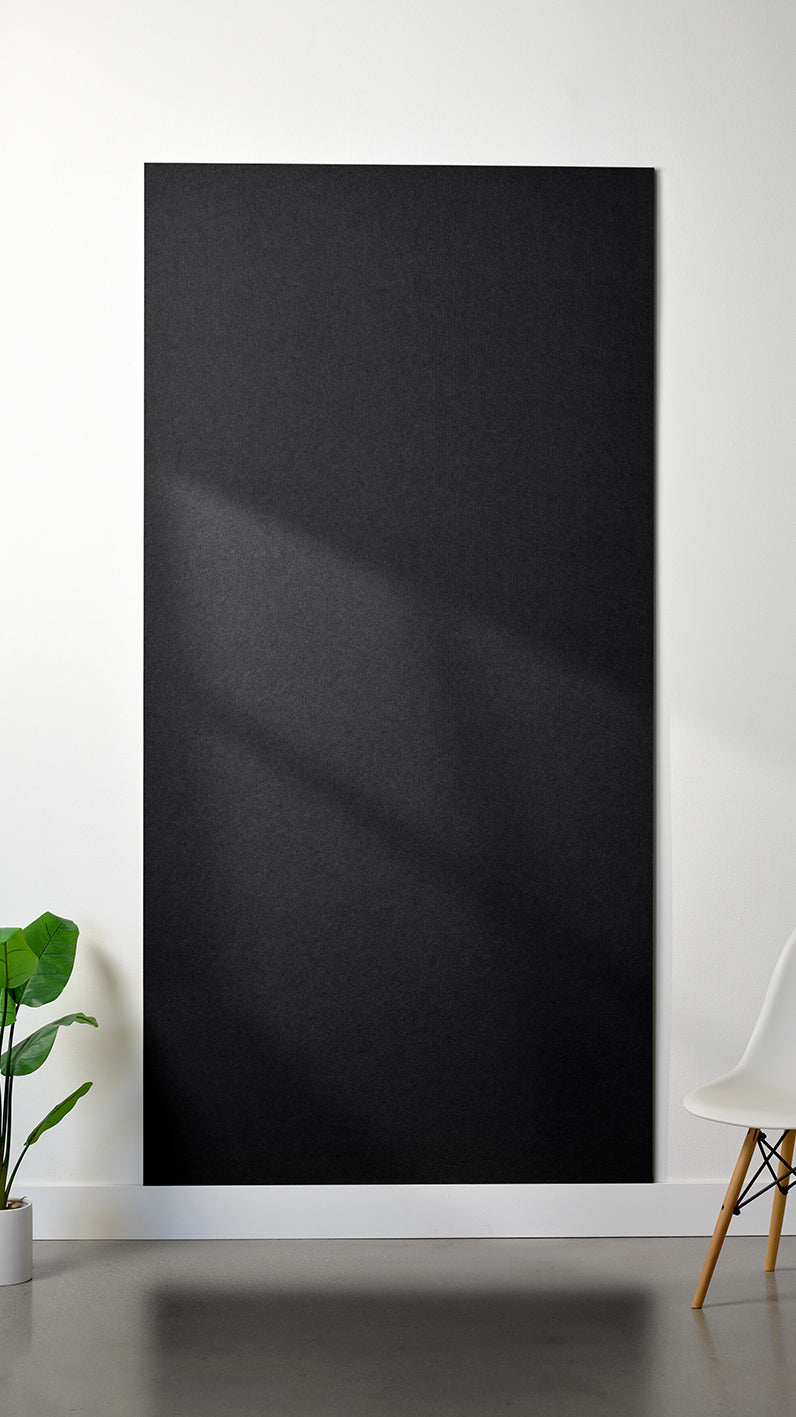 Black Felt Right 4’ x 8’ PET felt panel with no engraving against a white wall. A plant and chair are in the foreground.