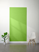 Fresh Lime colored 9mm acoustic felt wall panel on a white wall with a plant and chair in the foreground