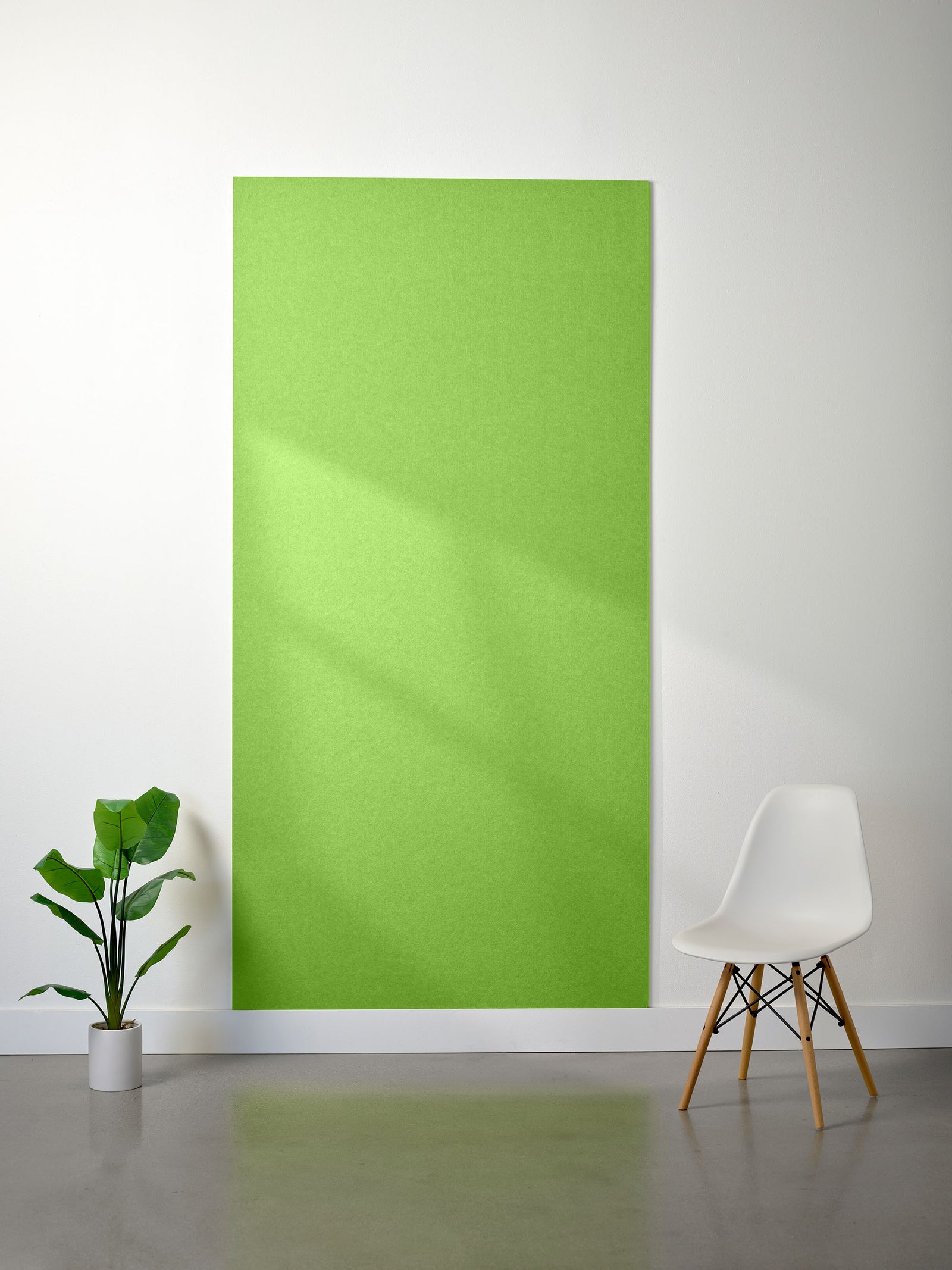 Fresh Lime colored 9mm acoustic felt wall panel on a white wall with a plant and chair in the foreground