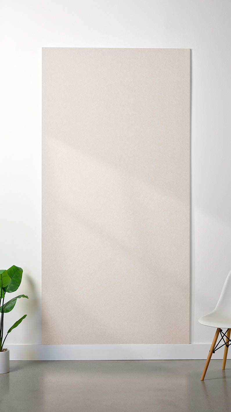 Heathered beige Felt Right 4’ x 8’ PET felt panel with no engraving against a white wall. A plant and chair are in the foreground.