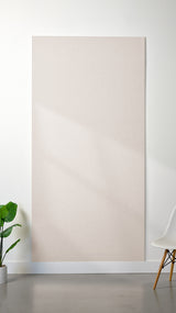 Heathered beige Felt Right 4’ x 8’ PET felt panel with no engraving against a white wall. A plant and chair are in the foreground.
