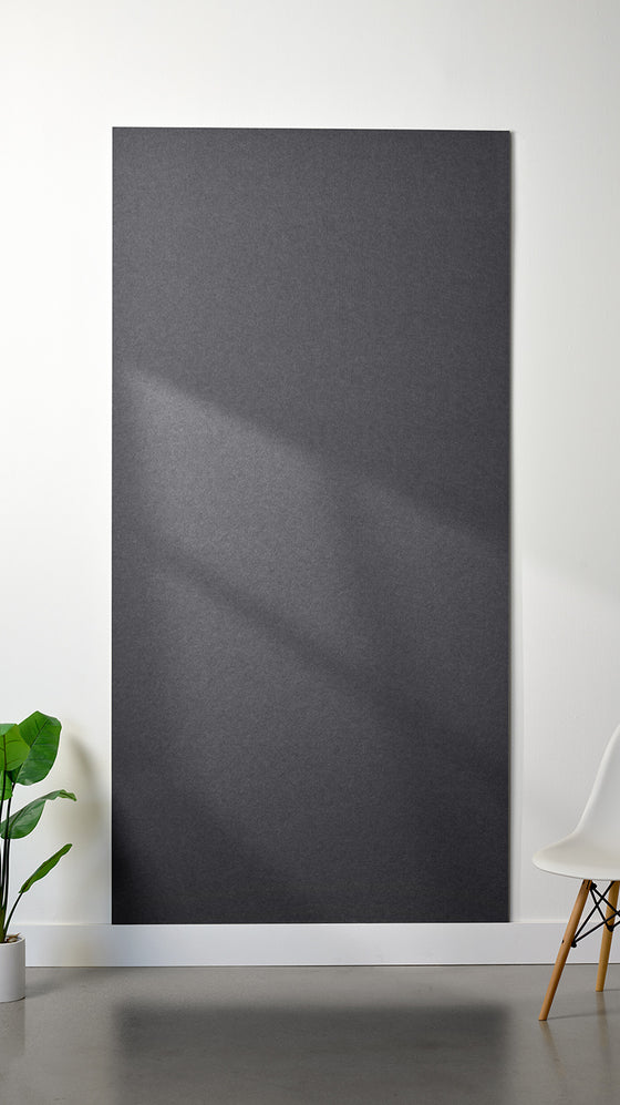 Grey Felt Right 4’ x 8’ PET felt panel with no engraving against a white wall. A plant and chair are in the foreground.