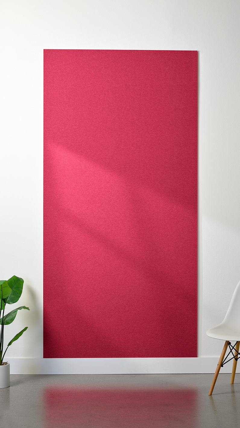 Bright red Felt Right 4’ x 8’ PET felt panel with no engraving against a white wall. A plant and chair are in the foreground.