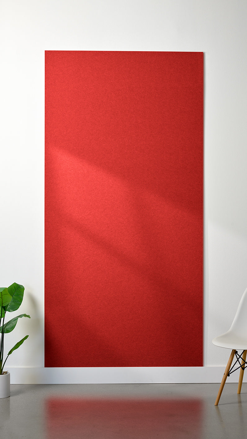 Red Felt Right 4’ x 8’ PET felt panel with no engraving against a white wall. A plant and chair are in the foreground.