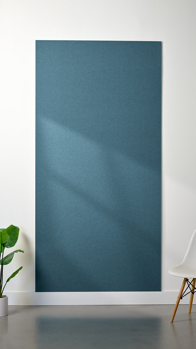 Blue Felt Right 4’ x 8’ PET felt panel with no engraving against a white wall. A plant and chair are in the foreground.