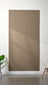 Light brown Felt Right 4’ x 8’ PET felt panel with no engraving against a white wall. A plant and chair are in the foreground.