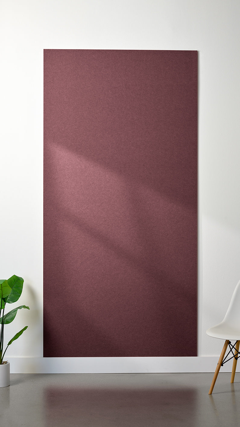 Maroon Felt Right 4’ x 8’ PET felt panel with no engraving against a white wall. A plant and chair are in the foreground.