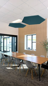 Two teal hexagonal acoustic panels suspended from ceiling in conference room above wooden table.