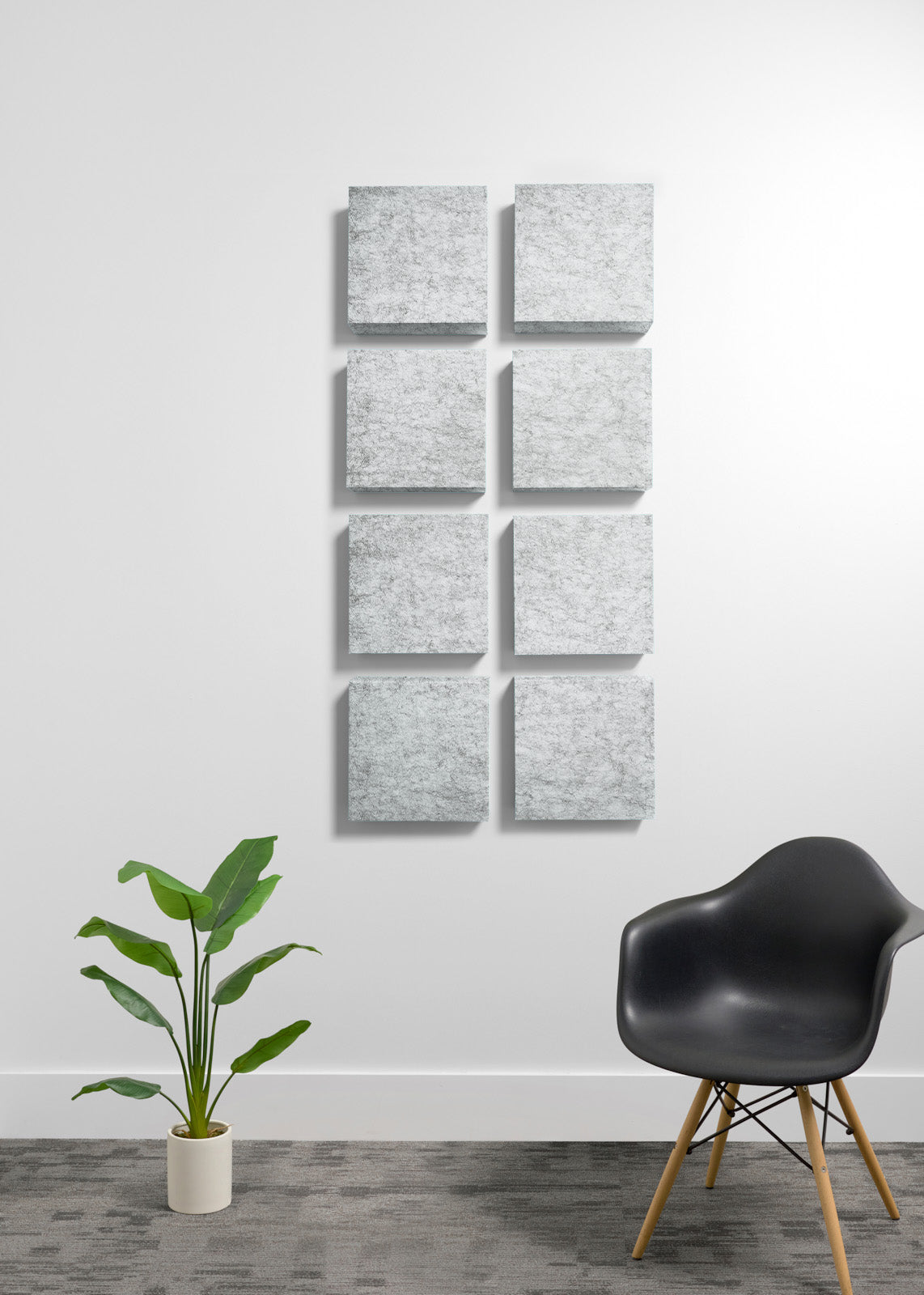A set of nine square gray textured wall panels arranged in a 3x3 grid on a white wall, with a potted green plant and a black molded chair in a modern room setting.