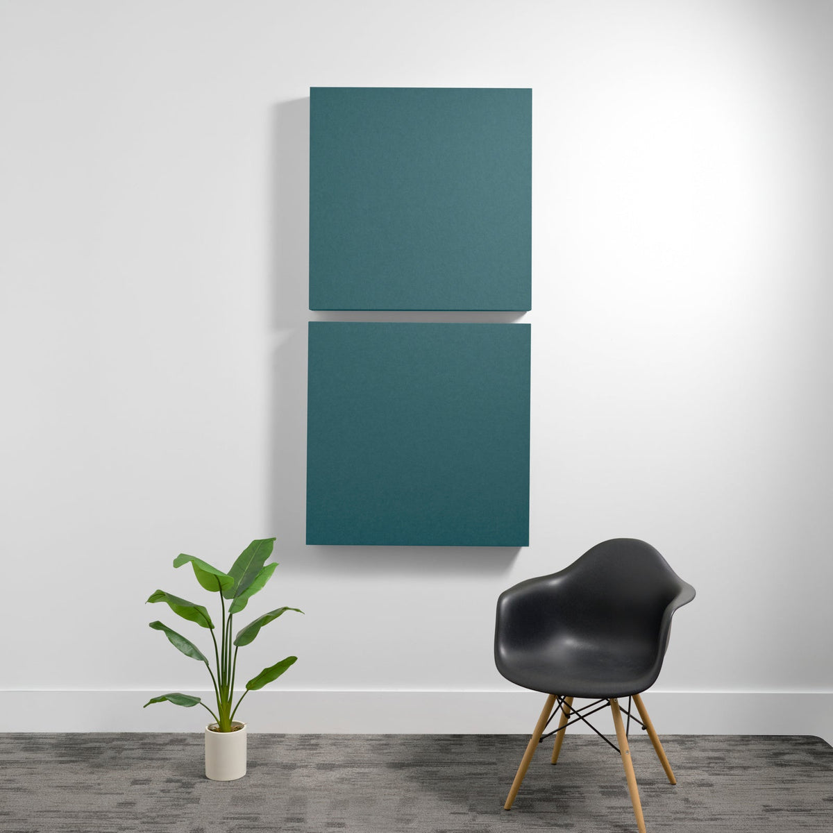 Two teal square acoustic panels mounted vertically on a white wall with a black chair and potted plant below.