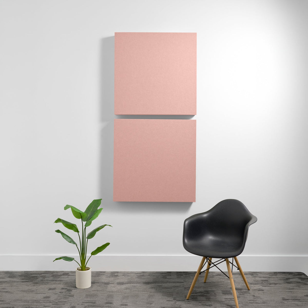 Two pink square acoustic panels mounted vertically on a white wall above a black chair and potted plant.