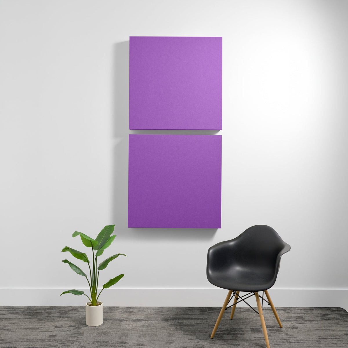 Two stacked purple acoustic panels mounted on a white wall above a black chair and potted plant.