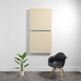 Two stacked cream-colored square acoustic panels mounted on wall above black chair and potted plant.