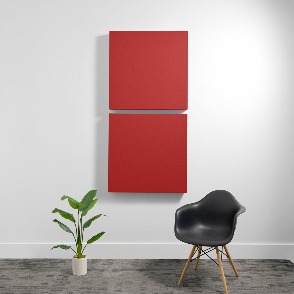 Two red square acoustic panels mounted vertically on a white wall above a black chair and potted plant.