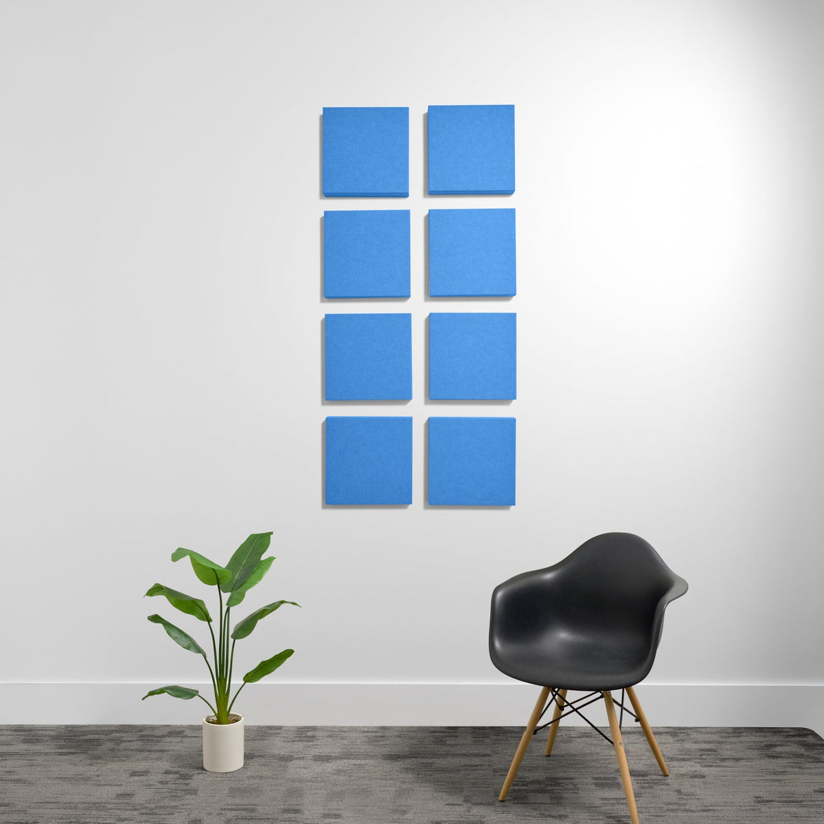 Eight blue square acoustic panels arranged in a 2x4 grid on a white wall above a black chair and potted plant.