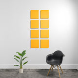 Eight yellow square acoustic panels arranged in a 2x4 grid on a white wall above a black chair and potted plant.