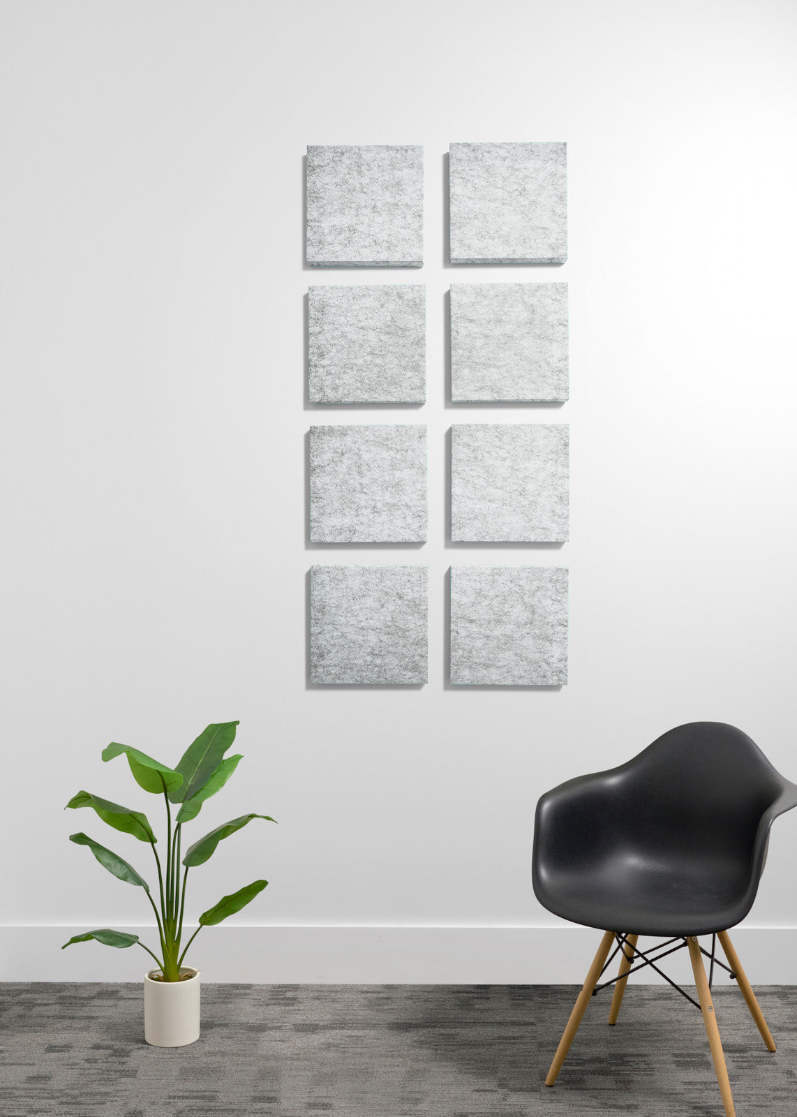 A set of eight square gray textured canvas prints arranged in two vertical columns of four on a white wall, styled in a modern room with a black chair and a green potted plant.