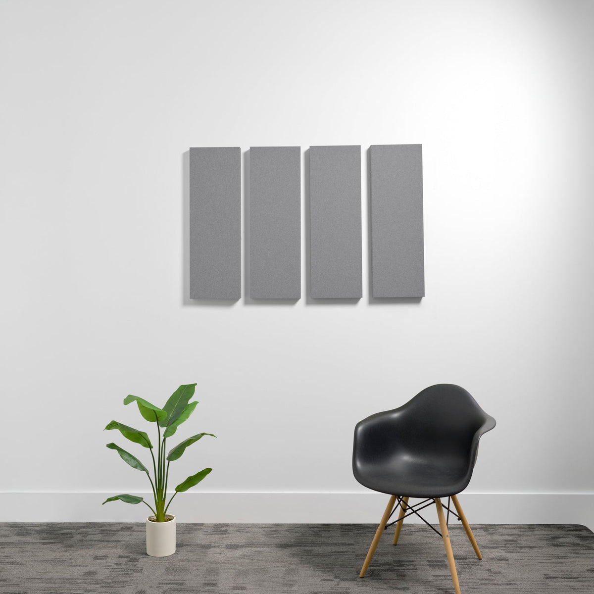 Four gray rectangular acoustic panels mounted on wall above plant and black chair.
