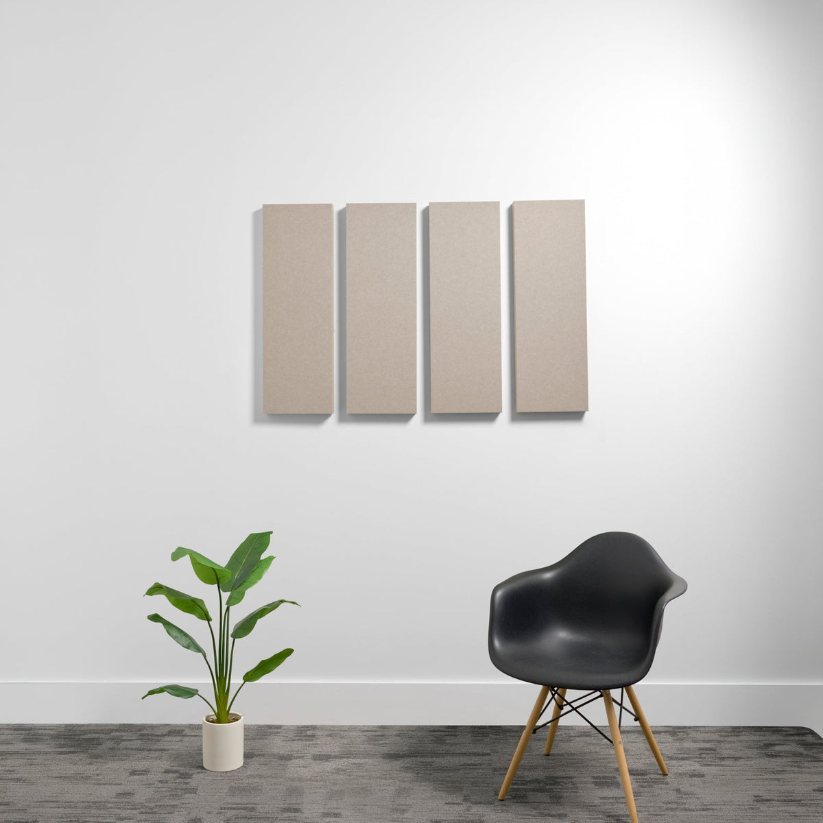 Four rectangular beige acoustic panels mounted on a white wall above a black chair and potted plant.